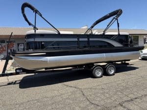 Luxury pontoon boat with black and silver finish, equipped with Bimini tops, on a dual-axle trailer.