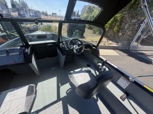 Boat cockpit with steering wheel and seating, outdoor marina setting.