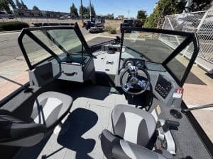 View of boat cockpit with steering wheel and control panel.