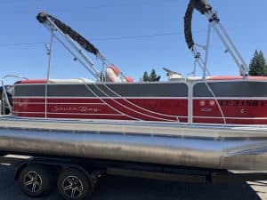 Red and white South Bay pontoon boat with Mercury engine on trailer.
