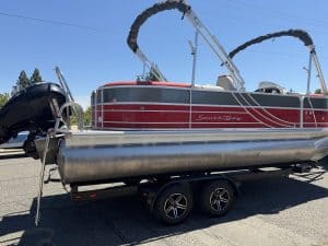 Pontoon boat with Mercury 150HP engine on trailer at dealership.