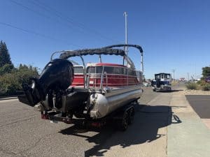 Pontoon boat with Mercury 150HP engine on trailer in parking lot.