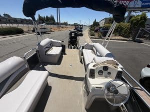 Pontoon boat with white seating and steering wheel on a sunny day.