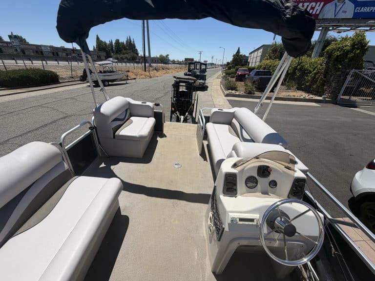 Pontoon boat with white seating and steering wheel on a sunny day.