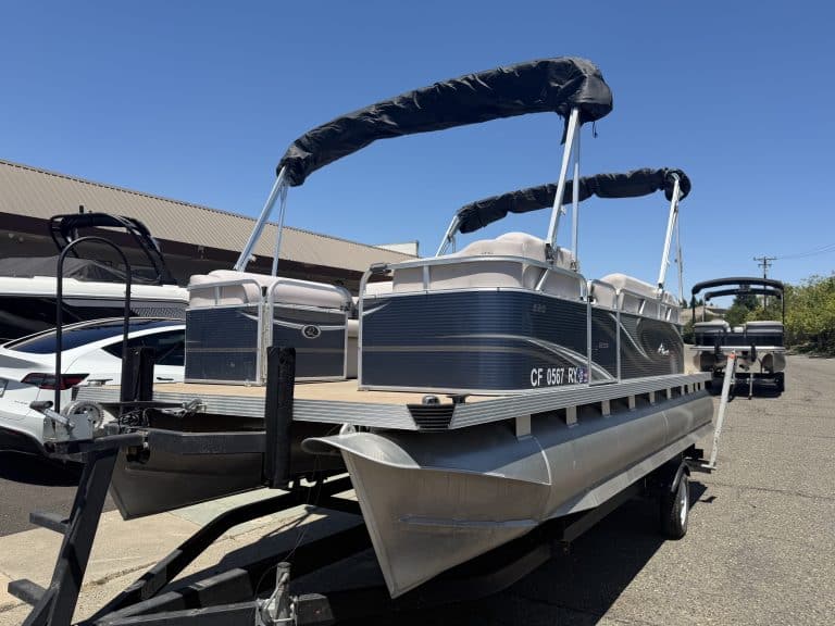 Pontoon boat with canopy on trailer at dealership lot.