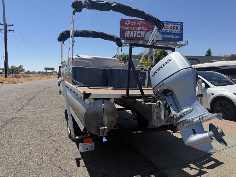 Pontoon boat with Honda outboard motor parked outdoors.