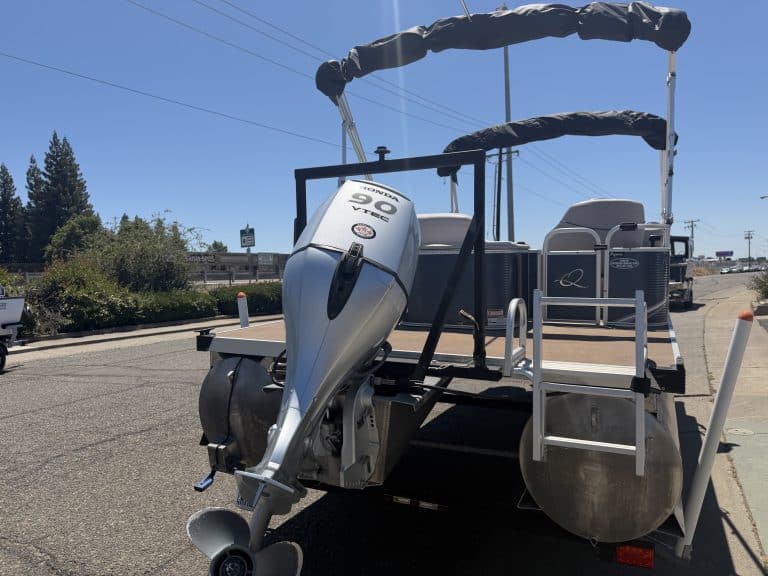 Pontoon boat with outboard motor on a road for sale or display.