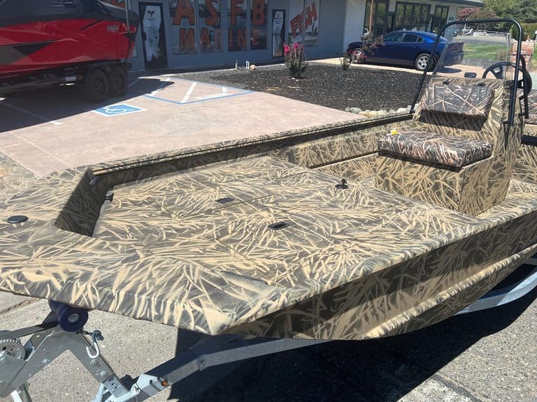 Camouflage fishing boat with seating and trolling motor in outdoor lot.