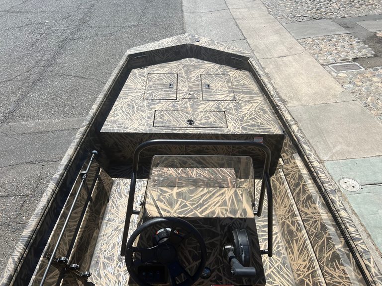 Camouflage boat with steering console and windshield for outdoor use.
