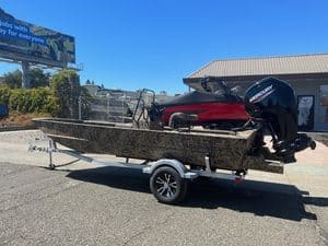 Camouflage Roughneck fishing boat with Mercury outboard motor on trailer.