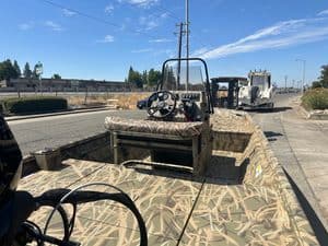 Camouflage boat with steering wheel and dashboard on a sunny day.