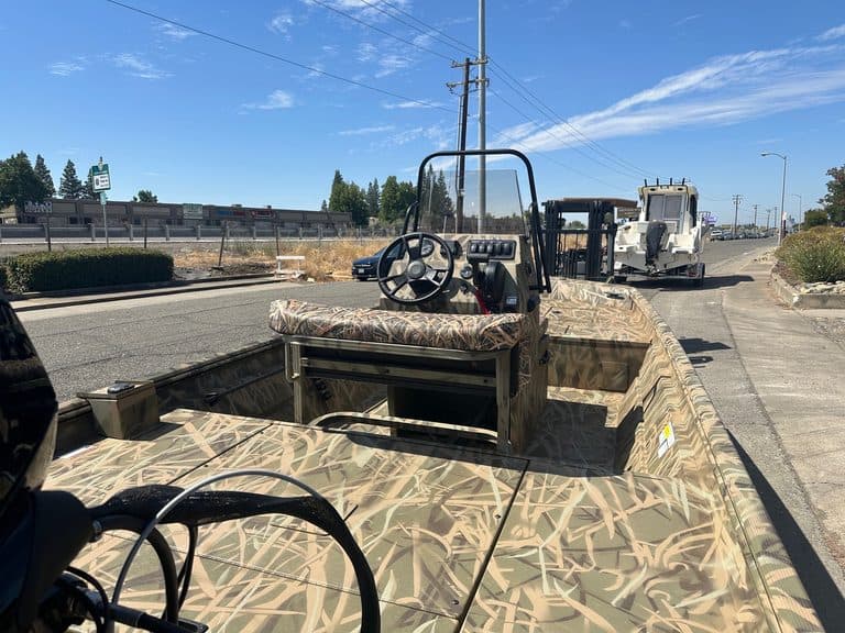 Camouflage boat with steering wheel and dashboard on a sunny day.