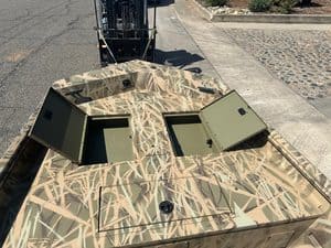 Camouflage boat with storage hatches and a forklift in the background.