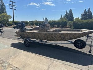Camouflage boat on trailer with outboard motor on a sunny day.