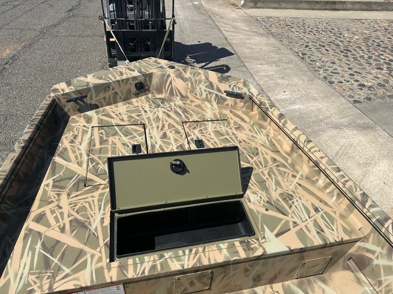 Camouflage boat with storage hatch and outboard motor at dock.