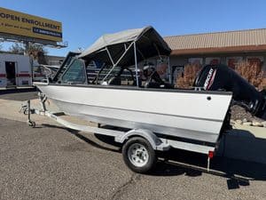 White motorboat with canopy on trailer at dealership lot.