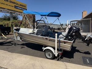 Westcoaster boat with outboard motor on trailer in parking lot.