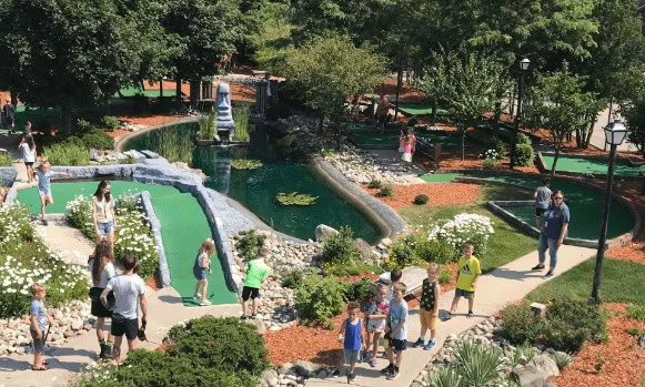 Children and families enjoying Bat'n Club park with water features and lush greenery.