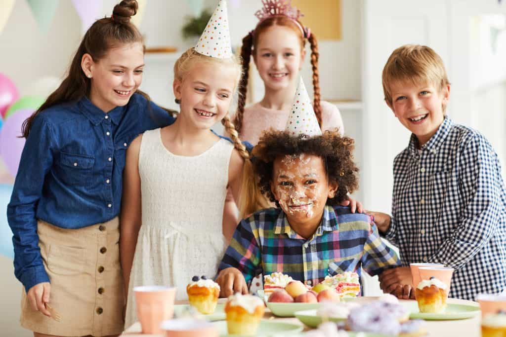 Children celebrating birthday with cake and party hats at Bat'n Club event.