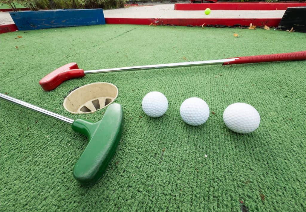 Miniature golf putters and balls on green artificial turf.