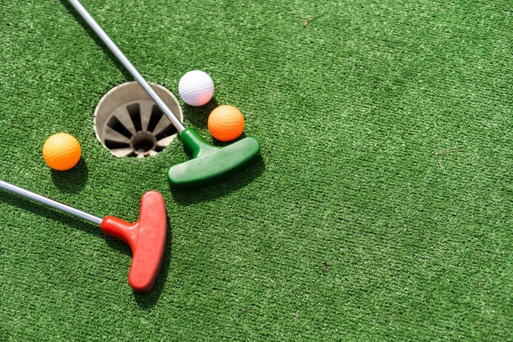 Mini golf putter and balls on green artificial turf.