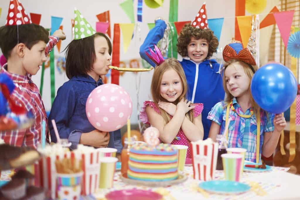 Children celebrating birthday with balloons and cake at Bat'n Club event.