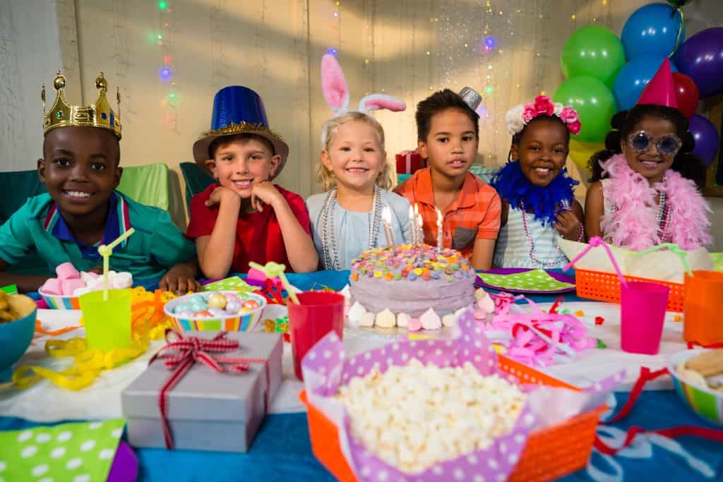 Children celebrating birthday with cake, balloons, and party hats at Bat'n Club.