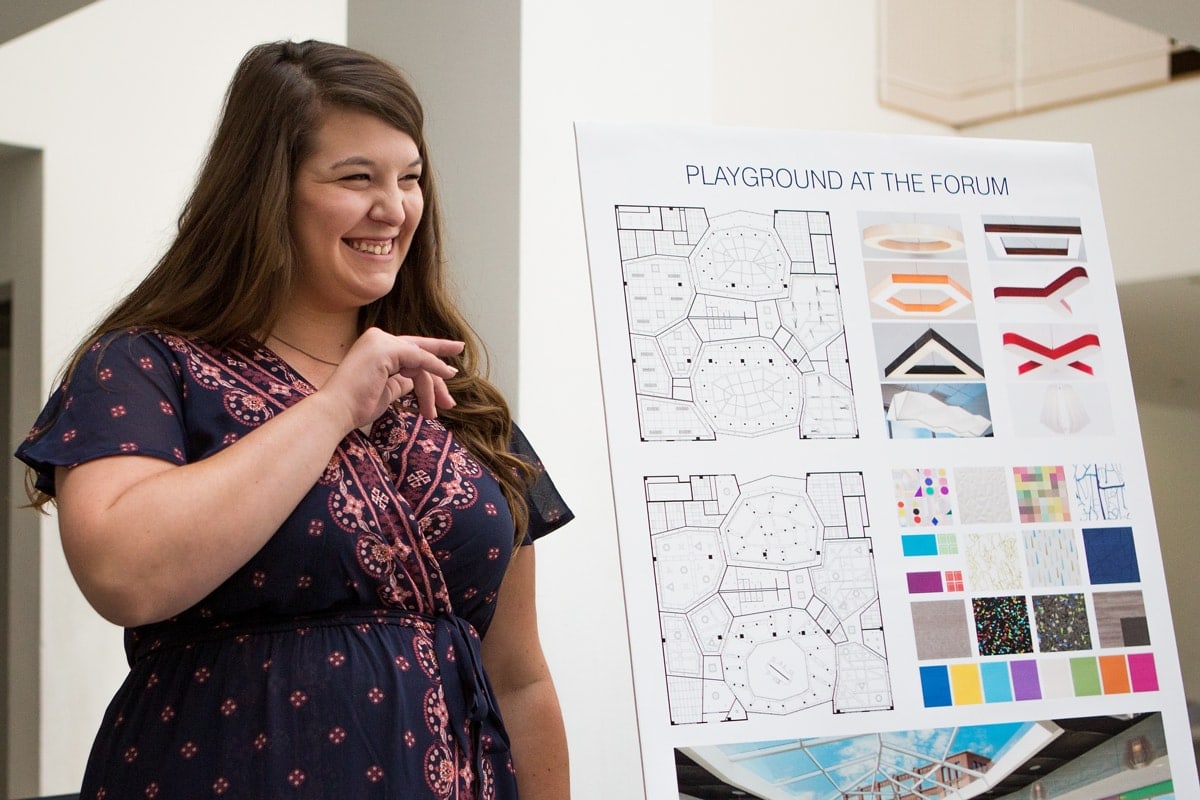 Katlyn Jarrard waves at family members while presenting her final portfolio during a Master of Interior Design portfolio show at the High Museum of Art in Atlanta. (AJ Reynolds/Brenau University)