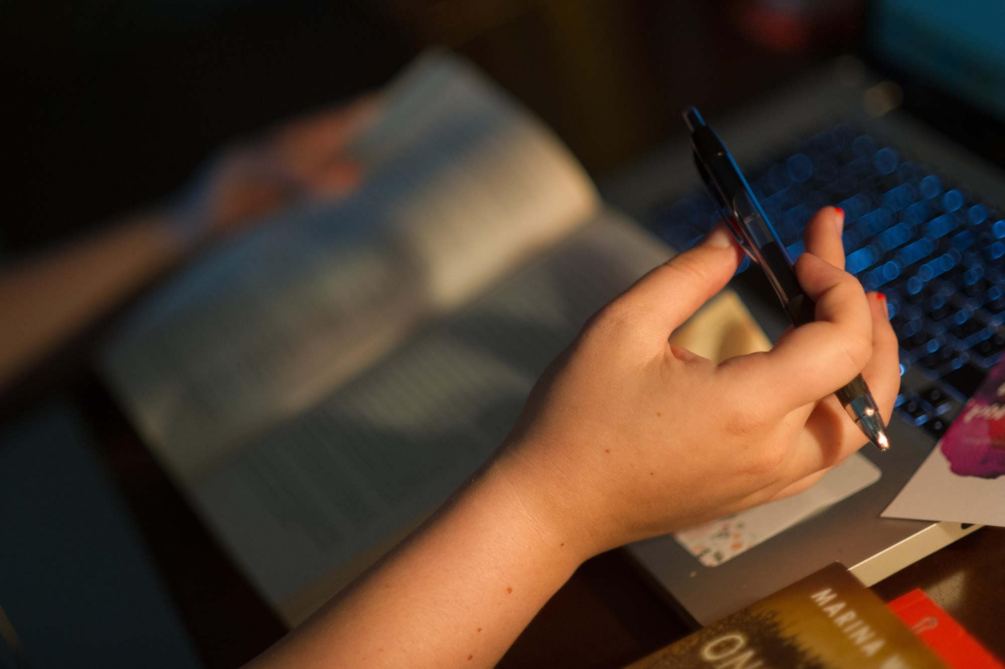 A hand seen in front of a book and laptop