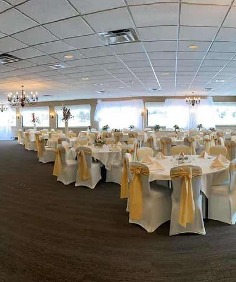 Banquet hall at Cascades Manor with round tables, white chair covers, and gold sashes for events.