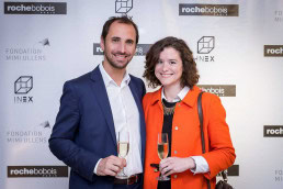 A couple smiles in front of a banner during an event for Roche Bobois Brussels