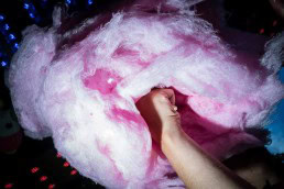 Close up flash street photograph of a big cotton candy from low perspective being held by a hand