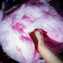 Close up flash street photograph of a big cotton candy from low perspective being held by a hand