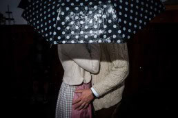 Close up flash street photograph of a couple having an intimate moment under a polka dot umbrella