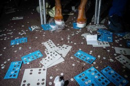 Close up flash street photograph of a woman's feet standing in front of many Bingo cartons
