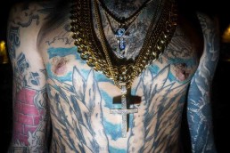Close up flash street photograph of a man's chest full of tattoos and with gold necklaces