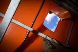 Close up flash street photograph of an orange tent with a hole from where the blue sky can be seen