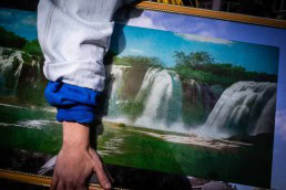 Close up flash street photograph of a someone's arm carrying a painting of a waterfall