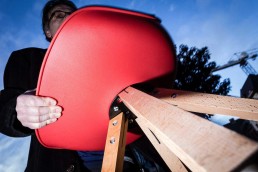 Close up flash street photograph of a man carrying a red chair seen from low perspective towards up