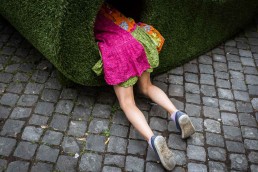 Street Photograph of a girl on a pink dress entering a hole in a green structure