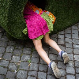 Street Photograph of a girl on a pink dress entering a hole in a green structure