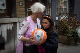 A woman carrying a ball next to a girl looking in the other direction in the streets