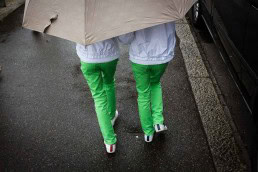 A couple of girls dressed with green pants and white sweatshirts covered by a large umbrella
