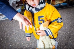 Close up flash street photograph of a child wearing a yellow jacket holding a teddy duck
