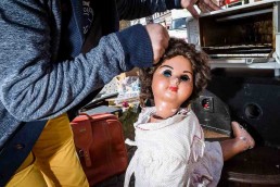 Close up flash street photograph of doll being held by her hair by someone's hand