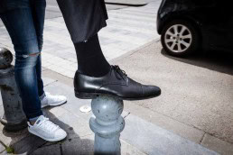 Close up flash street photograph of someone's foot wearing a black shoe on top of a street pole
