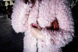 Close up flash street photograph of the torso of a woman wearing a pink fluffy coat