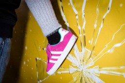 Close up flash street photograph of a child's foot wearing a pink shoe against a yellow wall