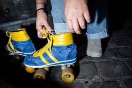 Close up flash street photograph of person fixing their blue and yellow roller skates