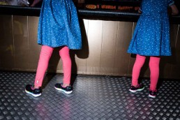 Close up flash street photograph of two girls seen from behind wearing blue dresses and pink socks